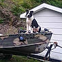 dog, boat, camouflage, trailer, grass, building, white_wall, hill, outdoor, pet, canine, animal, nature, yard, sitting, black_and_white, adventure, quiet, daytime, vehicle