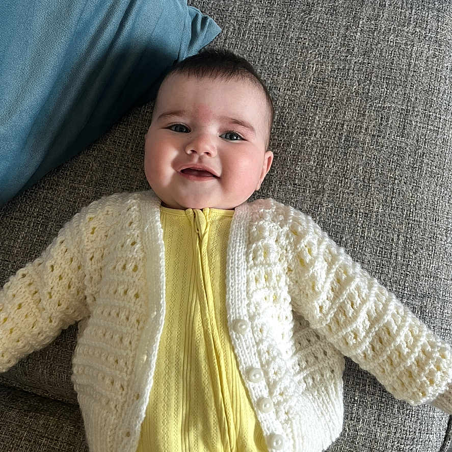 Maeve is registered to the contest to win money with this photo: baby, cardigan, clothing, couch, cushion, face, furniture, happy, hat, head, homedecor, knitwear, longsleeve, newborn, person, photography, portrait, sleeve, smile, sweater
