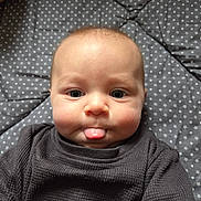 Oakley is registered to the contest to win money with this photo: baby, face, tongue, expression, sweater, clothing, infant, cute, cheeks, lying_down, blanket, stars, pattern, indoor, portrait, child, skin, head, playful, person