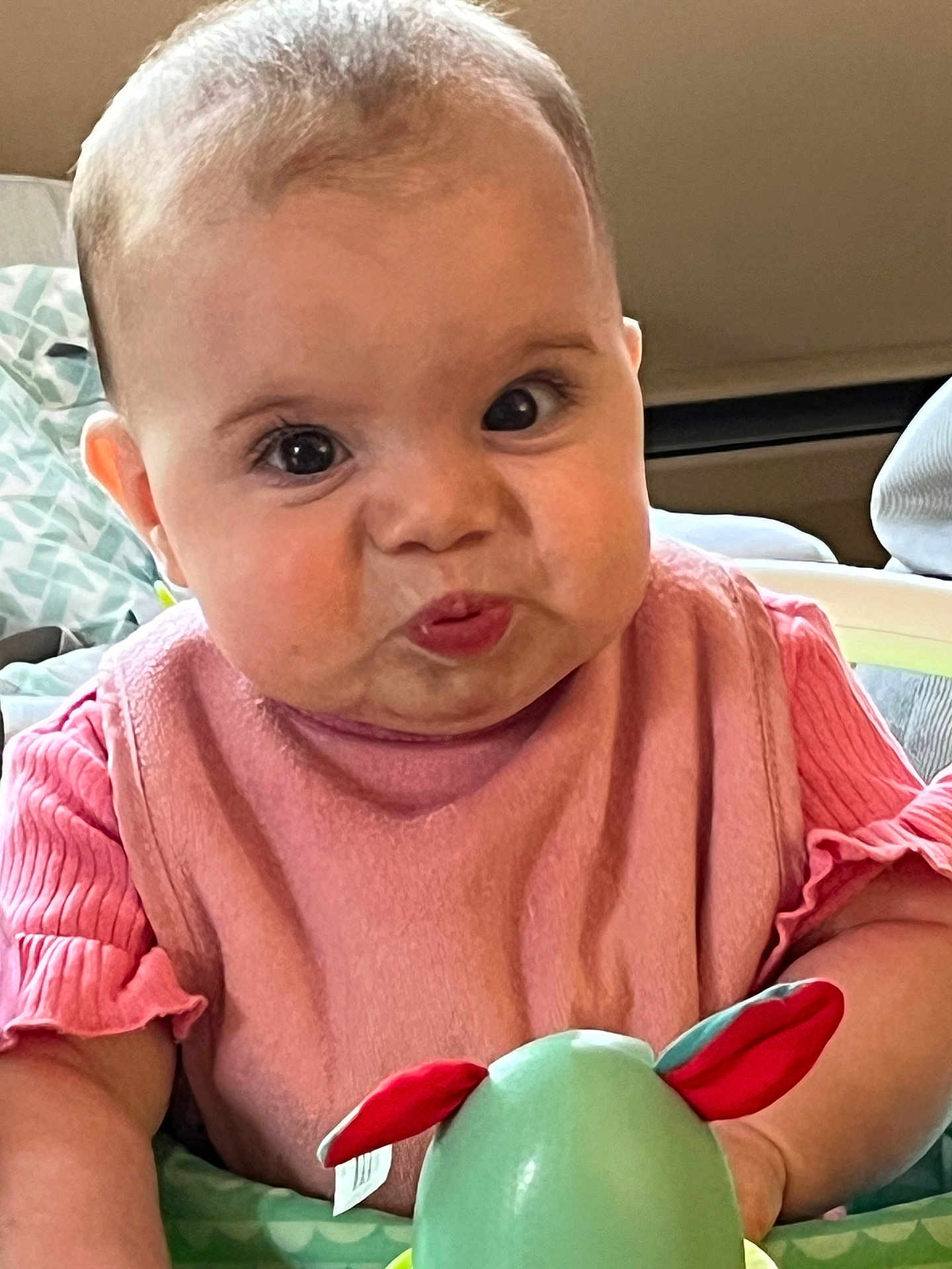 Paige Violet is registered to the contest to win money with this photo: baby, bib, cheeks, child, closeup, cushion, cute, expression, face, happy, head, indoor, infant, person, pink_clothing, playful, puckered_lips, seat, toy, young_child