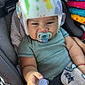 baby, infant, child, helmet, pacifier, car_seat, vehicle, sitting, portrait, face, hair, smiling, striped_shirt, blanket, colorful,  안전, indoors, close_up, infant_safety, travel