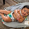 baby, infant, child, smiling, portrait, lying_down, bouncer, baby_seat, indoor, hardwood_floor, colorful_toy, rainbow, sun_design, monkey_design, diaper, bracelet, barefoot, happy, relaxed, photography