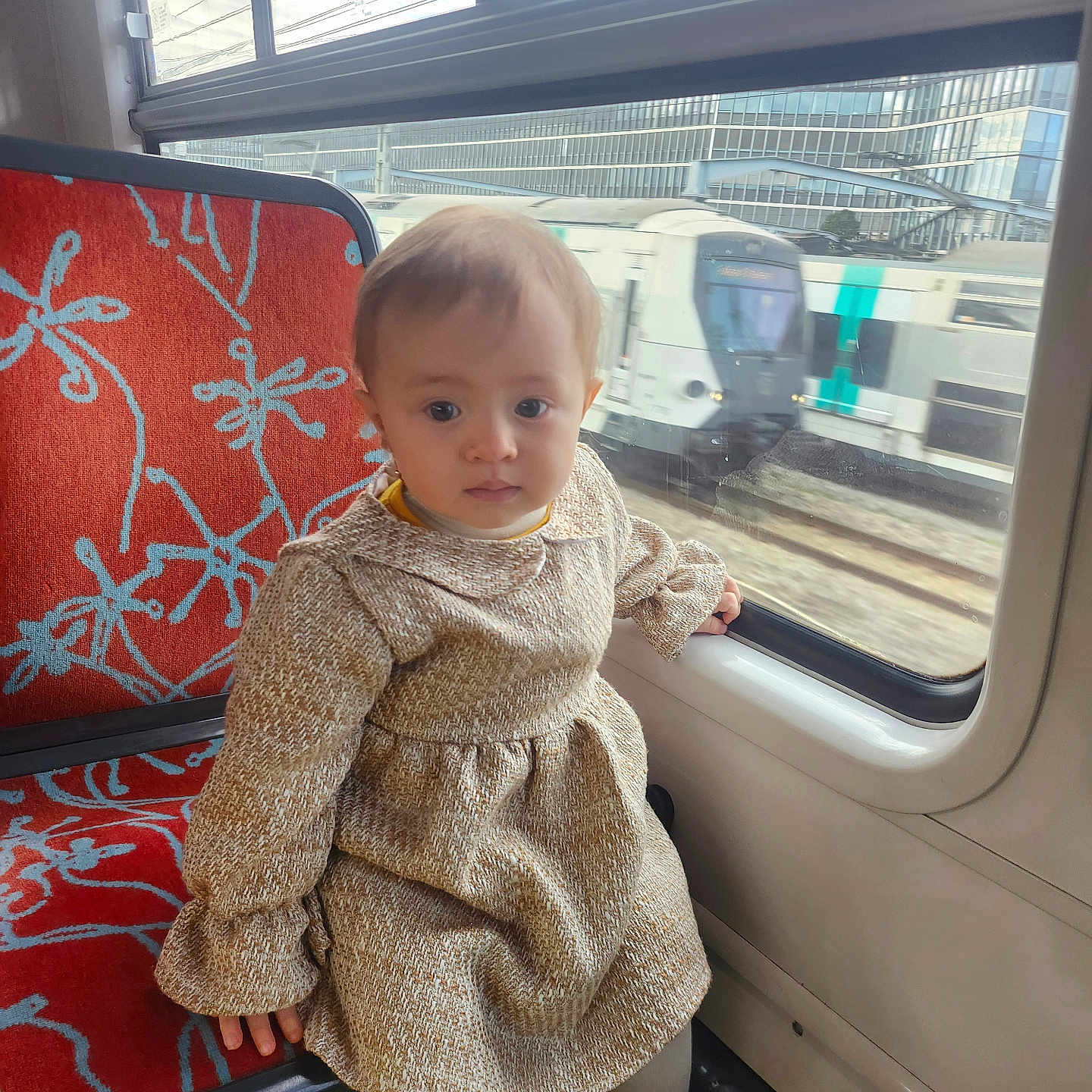 Sara participe au concours pour gagner de l'argent avec cette photo : beige, child, curious, daylight, dress, footwear, indoors, looking, pattern, person, public_transport, railway, red, seat, toddler, train, transport, travel, white_shoes, window
