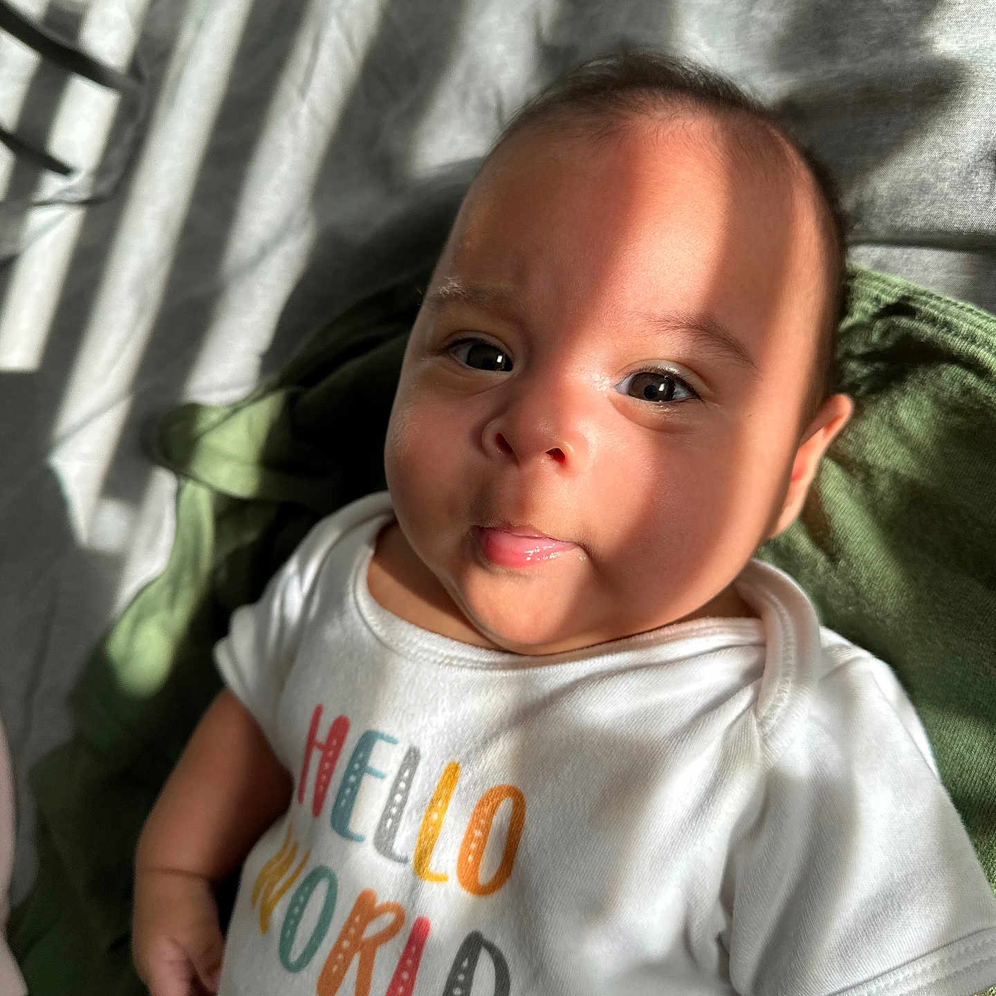 Jacqueline joined the competition — help win amazing prizes! baby, infant, child, onesie, clothing, text, hello_world, face, tongue, expression, sunlight, shadow, skin, eyes, indoor, blanket, green, white, cute, portrait