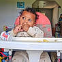 toddler, child, high_chair, pajamas, curly_hair, indoor, toys, foot, hand, face, expression, furniture, room, cozy, baby, casual_clothing, playtime, home, curiosity, seated