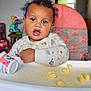 baby, high_chair, snack, cup, frozen_character, curly_hair, pajamas, indoor, child, face, expression, food, table, seat, toy, window, furniture, floor, person, home