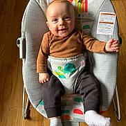 Kayden is registered to the contest to win money with this photo: baby, infant, smiling, baby_rocker, child, clothing, white_socks, wooden_floor, baby_toys, cute, happy, seated, indoor, portrait, face, head, playful, cozy, casual_wear, home
