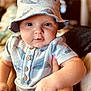 baby, infant, hat, bucket_hat, onesie, button_up, whale_pattern, hand, pink_nail_polish, face, eyes, cheeks, indoor, warm_lighting, person, portrait, cute, child, clothing, holding