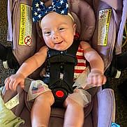 Azalea is registered to the contest to win money with this photo: baby, child, car_seat, headband, bow, clothing, smile, happy, infant, seatbelt, purple, indoor, playful, american_flag, tulle, feet, hands, person, cute, portrait