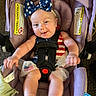 baby, child, car_seat, headband, bow, clothing, smile, happy, infant, seatbelt, purple, indoor, playful, american_flag, tulle, feet, hands, person, cute, portrait
