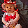 Azalea is registered to the contest to win money with this photo: baby, child, infant, smiling, red_bow, strawberry_pattern, sunhat, sitting, cute, clothing, hands, face, skin, person, portrait, indoors, fabric_background, summer_outfit, happy, playful