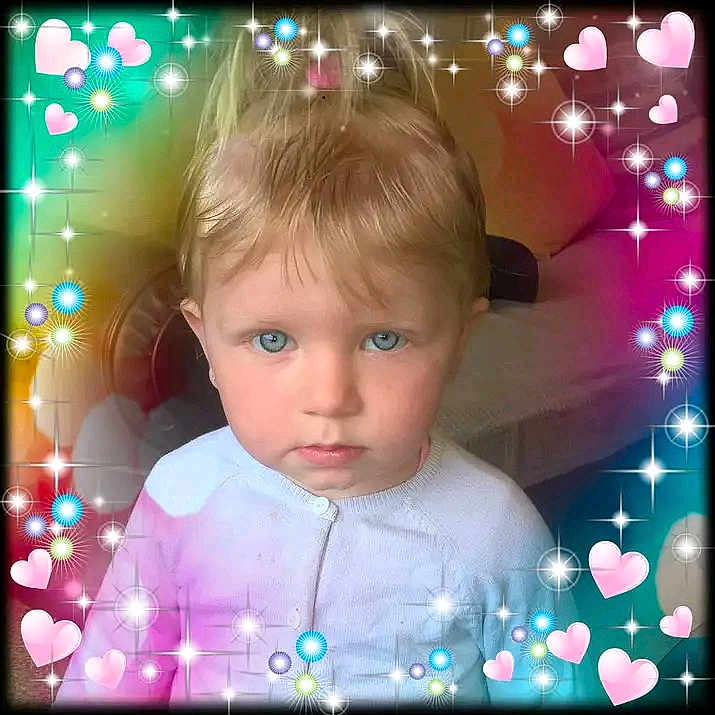 Jade a rejoint le concours — aidez-le/la à gagner de superbes lots ! baby, blonde_hair, blue_eyes, child, colorful, cute, decorative_border, face, frame, hearts, indoor, person, portrait, serious_expression, sofa, soft_lighting, sparkles, toddler, white_clothing, young_child