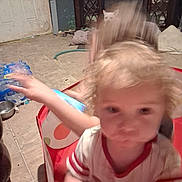 Jerry is registered to the contest to win money with this photo: child, toddler, face, blond_hair, blue_eyes, sitting, reaching, motion_blur, portrait, indoors, home, tiled_floor, furniture, cabinet, white_cat, bottled_water, toy, red_chair, casual_clothing, photograph