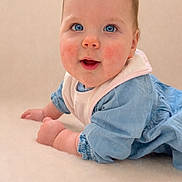 Esmée participe au concours pour gagner de l'argent avec cette photo : baby, infant, blue_eyes, rosy_cheeks, bib, blue_dress, cute, portrait, closeup, crawling, soft_background, studio_style, skin, face, hands, lying_down, young_child, innocent, smile, adorable