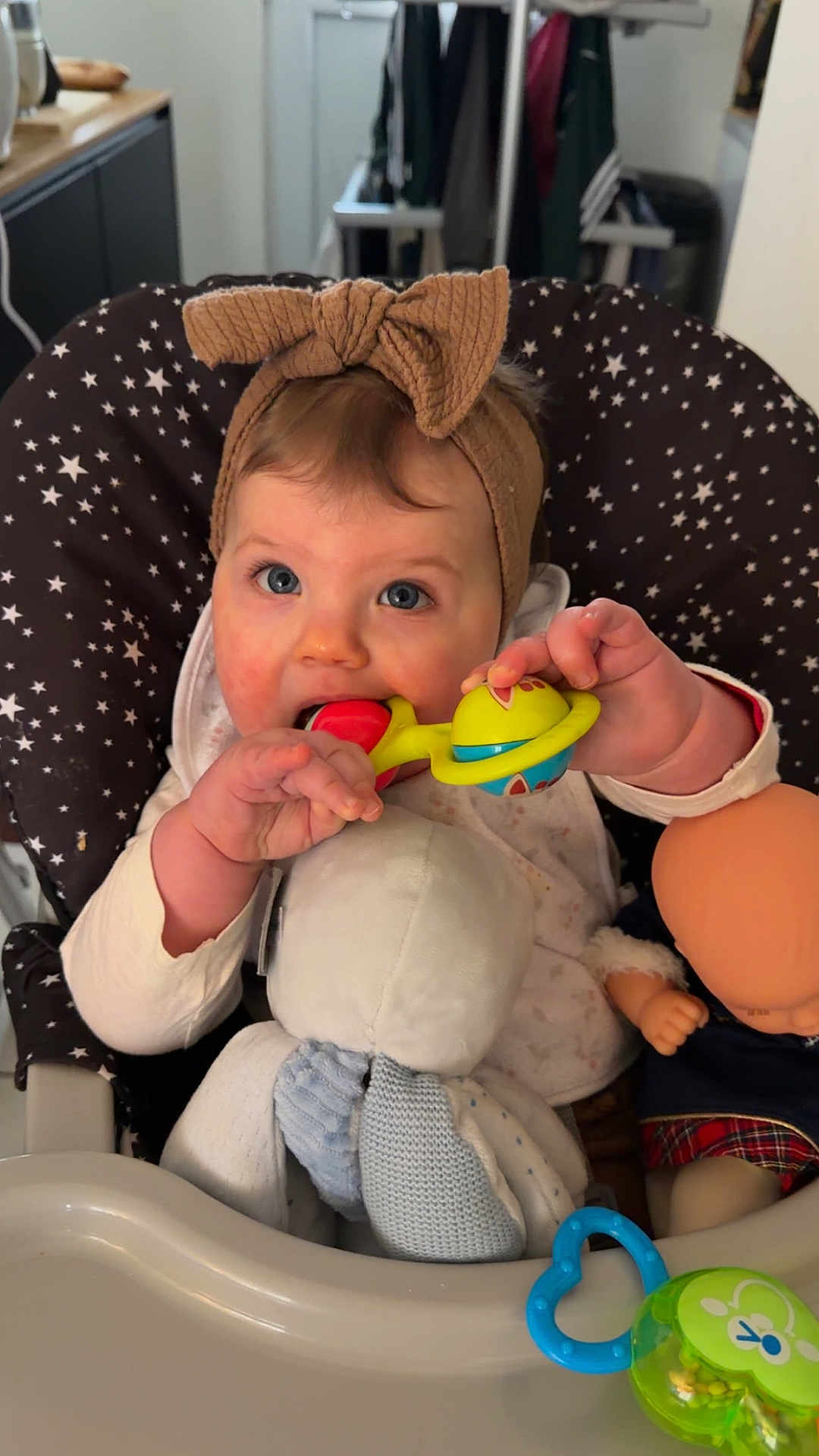 Esmée participe au concours pour gagner de l'argent avec cette photo : baby, infant, highchair, rattle, toy, plush_toy, doll, headband, bow, blue_eyes, teething, chewing_toy, star_pattern, tray, hands, mouth, clothing, indoor, kitchen_background, portrait