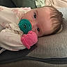 Lottie is registered to the contest to win money with this photo: baby, pacifier, mitten, cushion, face, infant, clothing, lying_down, indoor, closeup, head, soft_texture, pink, green, skin, person, newborn, blanket, comfort, rest