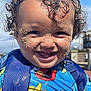 backpack, blue_sky, child, closeup, colorful_clothing, curly_hair, cute, daylight, face, happy, outdoor, person, playful, portrait, sand_on_face, sesame_street, smiling, sunny_day, toddler, young_child