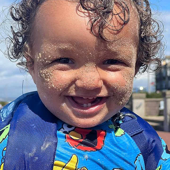 Elijah joined the competition — help win amazing prizes! backpack, blue_sky, child, closeup, colorful_clothing, curly_hair, cute, daylight, face, happy, outdoor, person, playful, portrait, sand_on_face, sesame_street, smiling, sunny_day, toddler, young_child