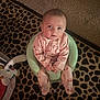 baby, infant, child, sitting, foam_seat, pajamas, onesie, carpet, leopard_print, rug, looking_up, eyes, face, hands, living_room, baby_bouncer, toy, cozy, carpet_pattern, portrait