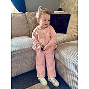 Grace Louise joined the competition — help win amazing prizes! toddler, child, pink_tracksuit, white_sneakers, sofa, couch, carpet, indoors, smiling, curly_hair, cozy, living_room, plush, casual_clothing, natural_light, person, home, cute, small_object, relaxed