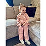 toddler, child, pink_tracksuit, white_sneakers, sofa, couch, carpet, indoors, smiling, curly_hair, cozy, living_room, plush, casual_clothing, natural_light, person, home, cute, small_object, relaxed