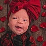 baby, infant, smiling, bow, headwrap, red, rose_petals, wooden_floor, floral_outfit, portrait, cute, happy, cheeks, eyes, closeup, newborn, headwear, fabric, rustic, texture