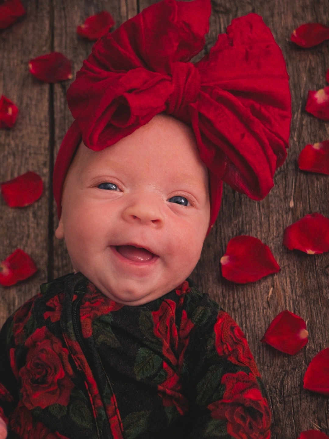 Saoirse joined the competition — help win amazing prizes! baby, infant, smiling, bow, headwrap, red, rose_petals, wooden_floor, floral_outfit, portrait, cute, happy, cheeks, eyes, closeup, newborn, headwear, fabric, rustic, texture