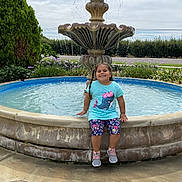 Adalyn is registered to the contest to win money with this photo: architecture, child, clothing, face, female, footwear, fountain, girl, head, person, photography, plant, pool, portrait, pottedplant, shoe, shorts, summer, swimmingpool, water