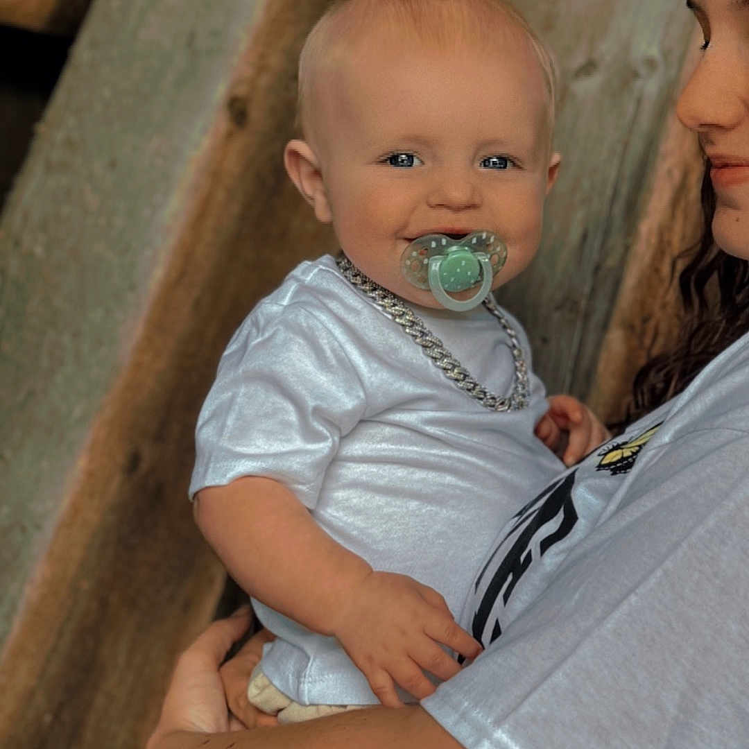 Kayssen is registered to the contest to win money with this photo: accessories, baby, bodypart, clothing, dress, face, finger, hand, happy, head, jewelry, necklace, pants, person, photography, portrait, sitting, smile, t_shirt, wood
