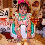 baby, baby_seat, birthday_cake, candle, celebration, child, colorful, cute, decorated_background, fabric, face, floral_outfit, foot, horse_toy, indoor, pillow, pink_bow, plush_toy, sitting, table