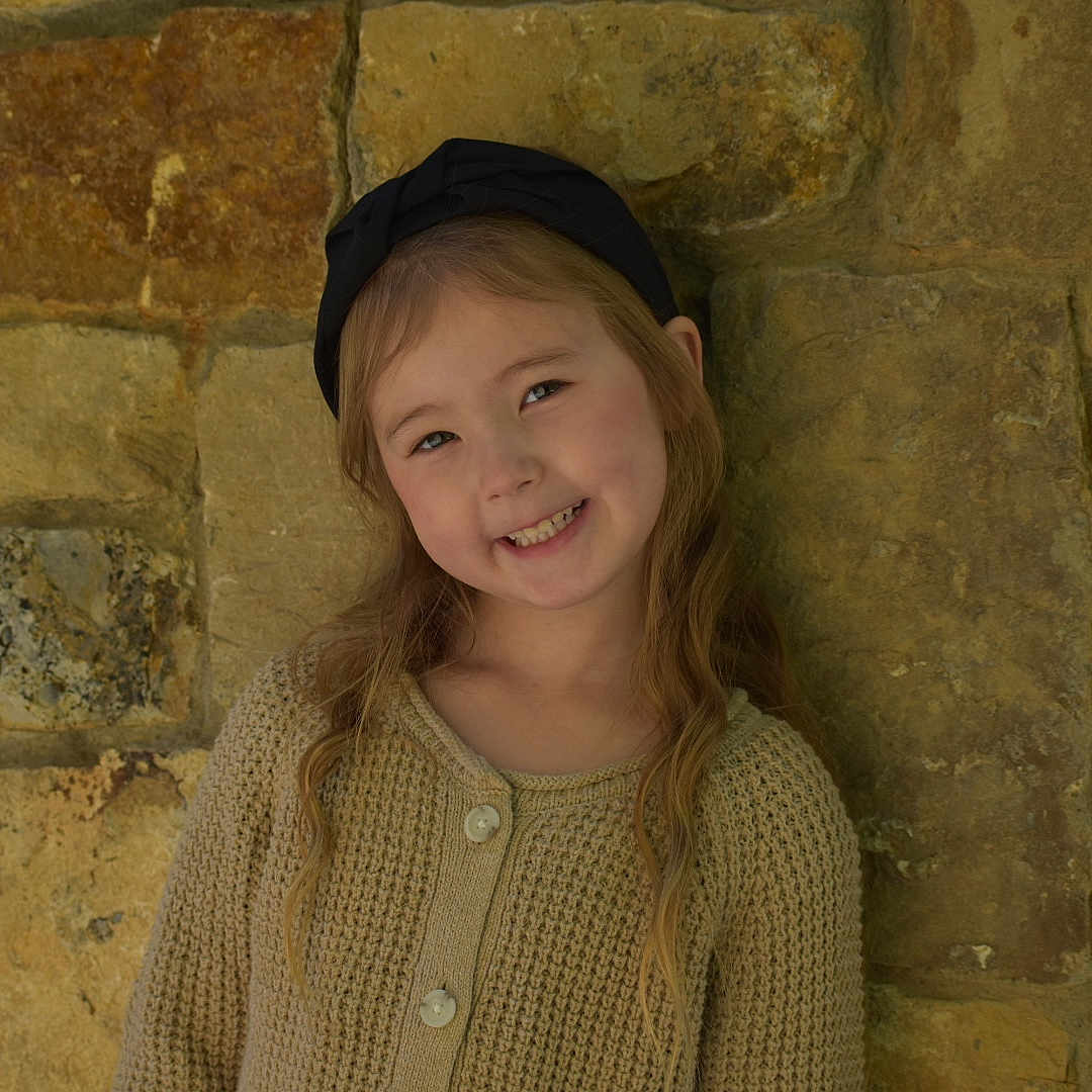 Stella is registered to the contest to win money with this photo: architecture, brick, building, cap, child, clothing, face, female, girl, happy, hat, head, knitwear, person, photography, portrait, smile, sweater, sweatshirt, wall