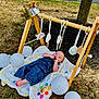 baby, denim_overalls, wooden_play_gym, hanging_toys, white_balloons, blanket, outdoor, grass, tree, sunny, child, infant, toy, crown, playtime, cute, relaxing, nature, happy, portrait