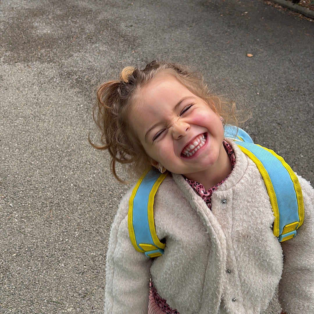 Ghita a rejoint le concours — aidez-le/la à gagner de superbes lots ! backpack, candid, child, coat, concrete, curly_hair, girl, happy, joyful, outdoor, pavement, pink_boots, playful, portrait, school_age, shrubbery, smiling, teeth, urban, winter_clothing