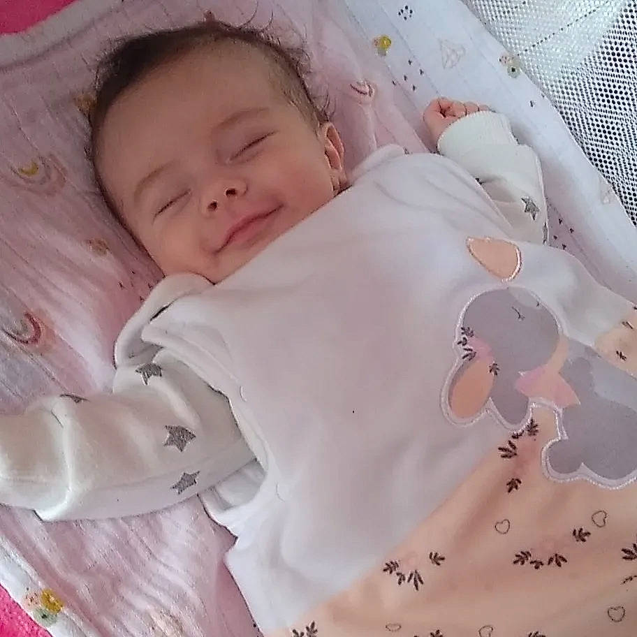 Dora participe au concours pour gagner de l'argent avec cette photo : baby, baby_products, baby_sleeping, baby_toddler_clothing, cheek, child, collar, comfort, eye, face, head, linens, pattern, peach, person, pink, skin, sleeve, smile, toddler