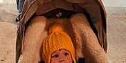 Eric joined the competition — help win amazing prizes! baby, child, stroller, blanket, hat, yellow_hat, pom_pom, toy, wooden_beads, face, eyes, hand, clothing, warm, indoor, floor, people, walking, person, curious