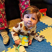 Eric is registered to the contest to win money with this photo: baby, child, onesie, toy, floor_mat, pajamas, socks, person, indoor, carpet, couch, hand, face, smile, cute, play, colorful, soft_toy, floor, seated