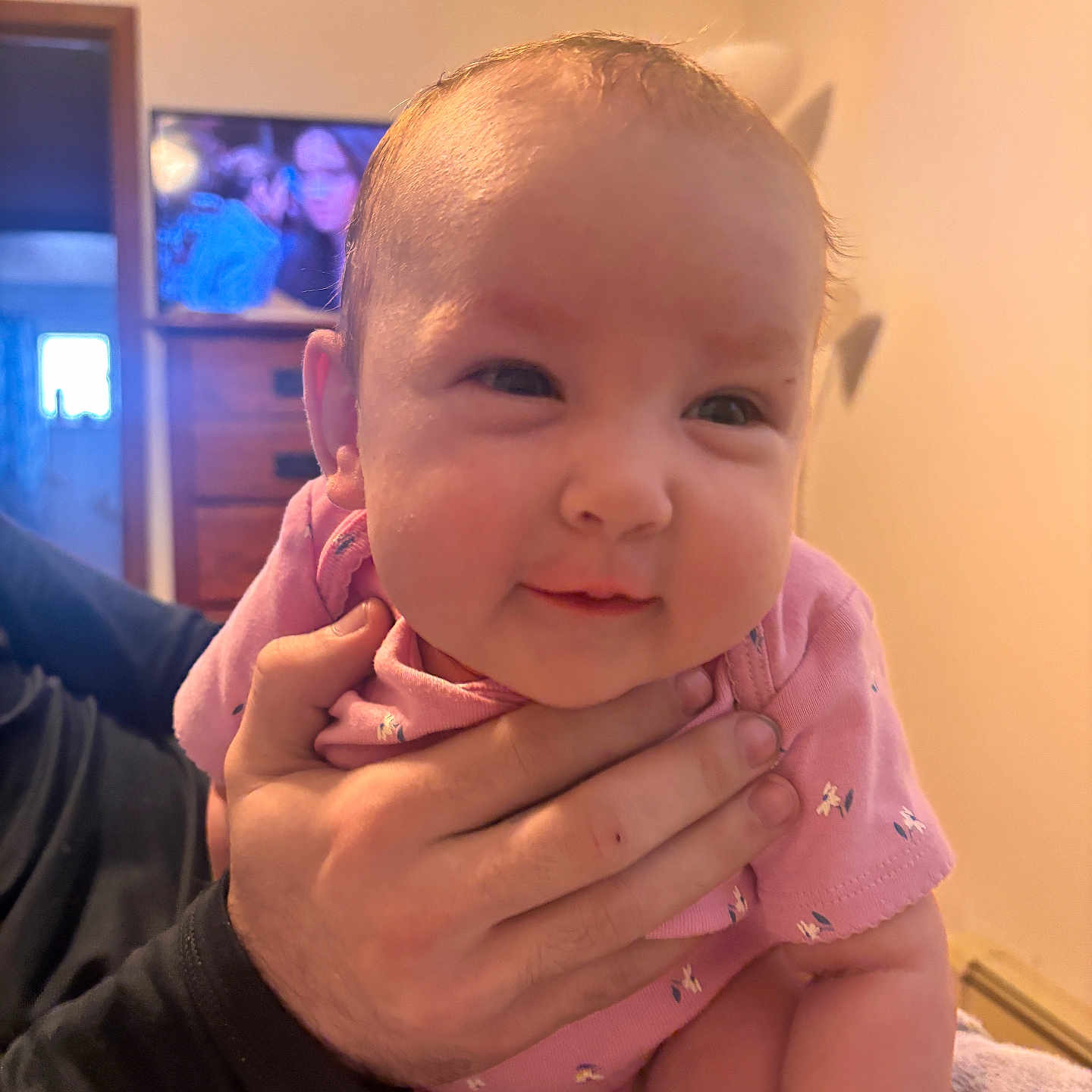 Amarianna joined the competition — help win amazing prizes! adult_hand, arm, baby, child, cozy, cute, face, furniture, hand, holding, human, indoor, infant, living_room, person, pink_clothing, skin, smile, soft_light, television