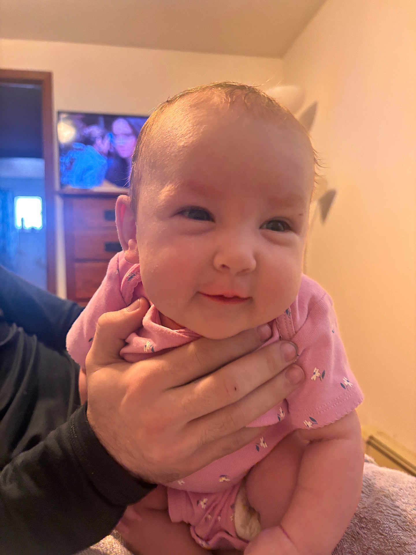 Amarianna joined the competition — help win amazing prizes! baby, infant, child, person, hand, pink_clothing, face, indoor, furniture, television, living_room, smile, cute, human, skin, arm, adult_hand, holding, soft_light, cozy