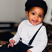 Mayson Da Veiga a rejoint le concours — aidez-le/la à gagner de superbes lots ! baby, child, smiling, hat, bib, suspenders, white_clothing, black_clothing, sitting, indoors, portrait, cute, happy, patterned_blanket, footwear, person, infant, closeup, fashion, young_child