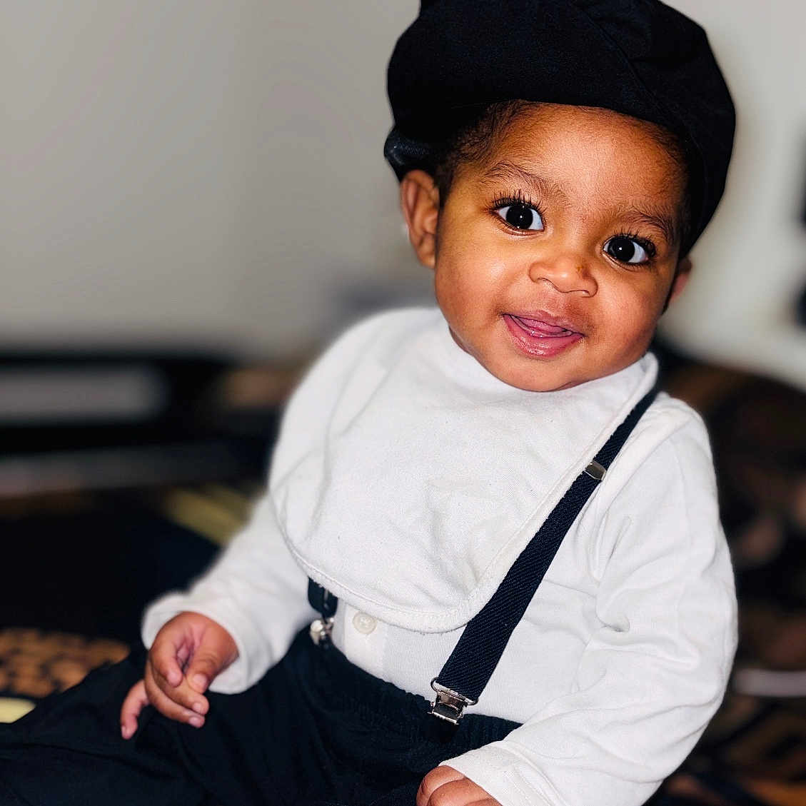 Mayson Da Veiga a rejoint le concours — aidez-le/la à gagner de superbes lots ! baby, bib, black_clothing, child, closeup, cute, fashion, footwear, happy, hat, indoors, infant, patterned_blanket, person, portrait, sitting, smiling, suspenders, white_clothing, young_child
