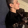 person, dog, black_dog, couch, indoor, snuggling, paws, earrings, short_hair, relaxing, face_profile, pet, companion, home, comfort, casual, black_clothing, resting, closeup, affection