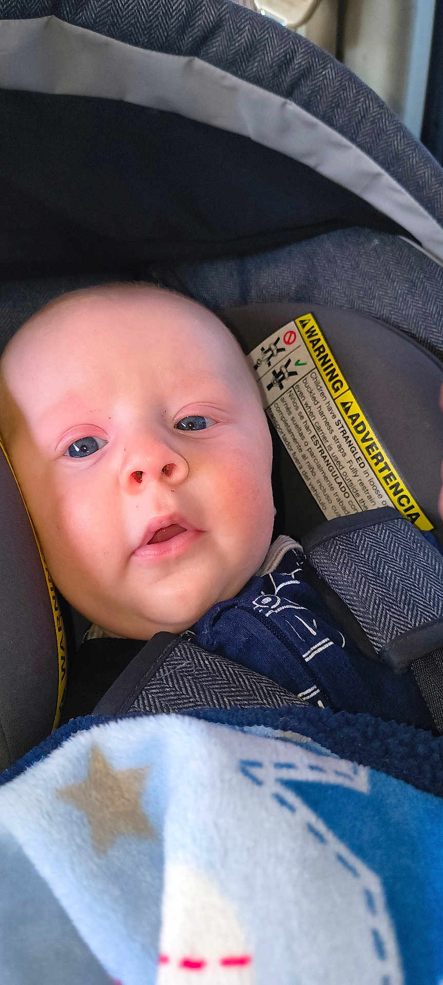 Nova Lane is registered to the contest to win money with this photo: baby, infant, child, face, eyes, nose, mouth, car_seat, seat_strap, canopy, warning_label, blanket, star_pattern, blue_blanket, clothing, portrait, close_up, soft_texture, fabric, cute