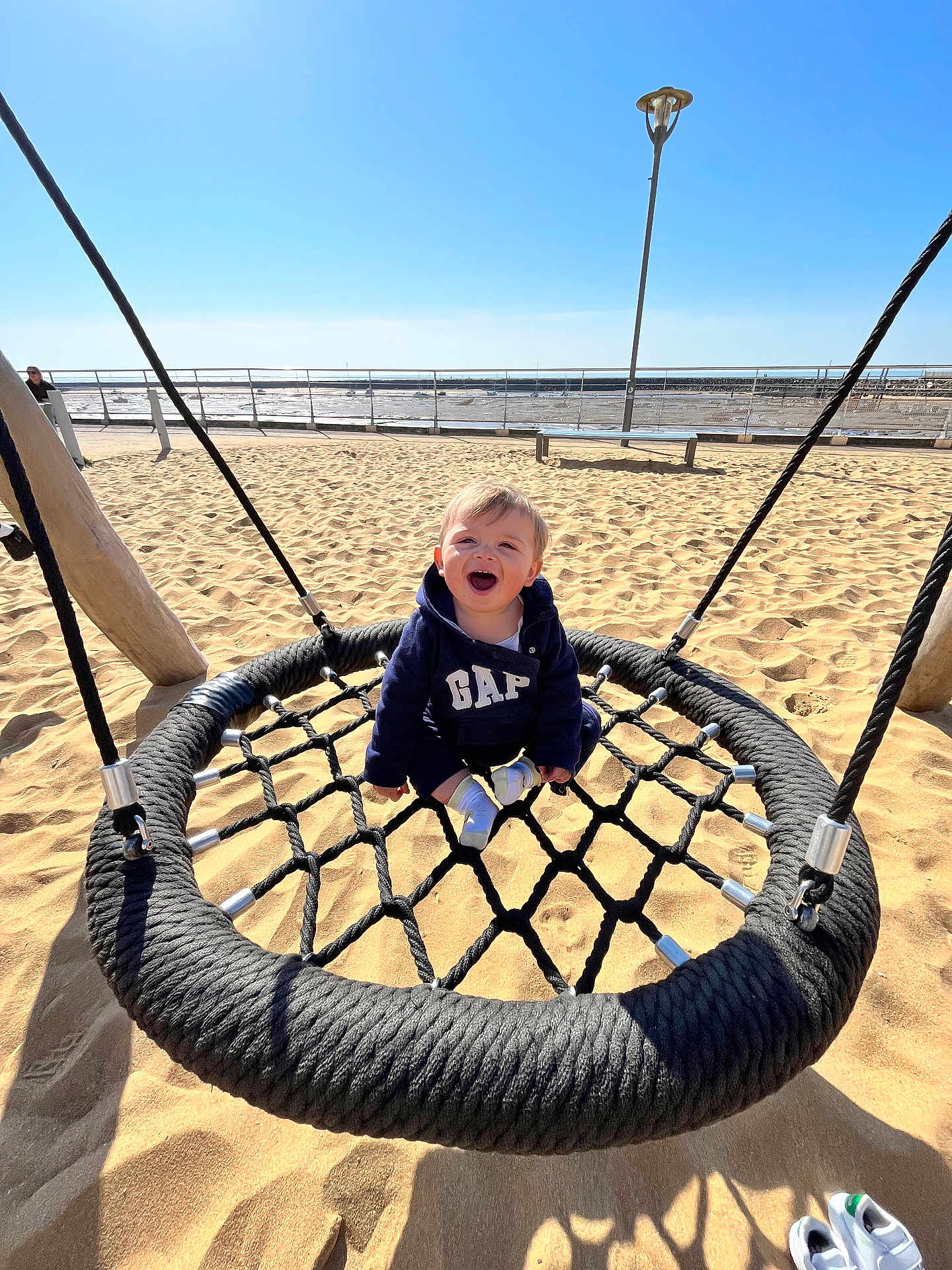 Marceau a rejoint le concours — aidez-le/la à gagner de superbes lots ! child, toddler, swing, playground, beach, sand, smiling, happy, rope, net_swing, hoodie, gap_hoodie, shoes, sunny, ocean, seaside_rail, lamp_post, shadow, play_equipment, cute