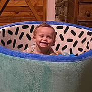Saige is registered to the contest to win money with this photo: toddler, child, play, ball_pit, plush, indoor, wooden_wall, stone_wall, smile, happy, face, hair, toy, cabin, cozy, person, furniture, colorful, cute, young