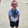 Kai is registered to the contest to win money with this photo: child, boy, smiling, standing, sidewalk, outdoor, sunny, shorts, tshirt, crocs, hairstyle, mohawk, hands_in_pockets, shadow, trees, casual_clothing, happy, person, daylight, concrete