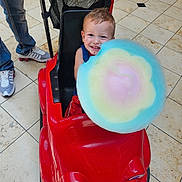 Kai is registered to the contest to win money with this photo: toddler, child, toy_car, cotton_candy, red, smiling, happy, indoor, floor, tiles, person, jeans, sneakers, playful, cute, food, snack, candy, colorful, fun
