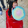 toddler, child, toy_car, cotton_candy, red, smiling, happy, indoor, floor, tiles, person, jeans, sneakers, playful, cute, food, snack, candy, colorful, fun