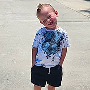 Kai is registered to the contest to win money with this photo: child, boy, smiling, outdoor, sunny_day, tshirt, shorts, red_shoes, concrete, sidewalk, hands_in_pockets, happy, casual_clothing, short_hair, portrait, standing, daylight, shadow, playful, young