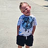 child, boy, smiling, outdoor, sunny_day, tshirt, shorts, red_shoes, concrete, sidewalk, hands_in_pockets, happy, casual_clothing, short_hair, portrait, standing, daylight, shadow, playful, young