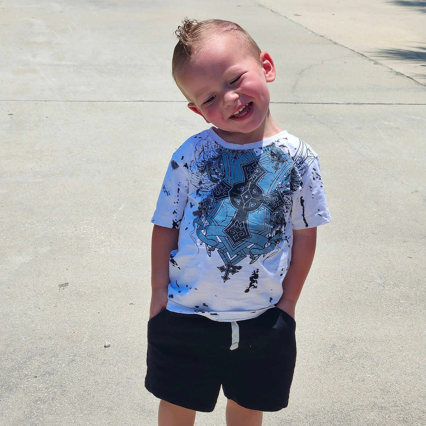 Kai is registered to the contest to win money with this photo: child, boy, smiling, outdoor, sunny_day, tshirt, shorts, red_shoes, concrete, sidewalk, hands_in_pockets, happy, casual_clothing, short_hair, portrait, standing, daylight, shadow, playful, young